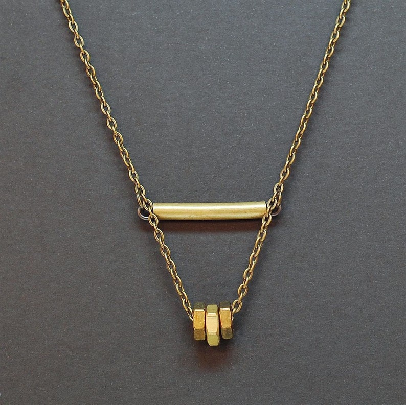 May include: A gold chain necklace with a horizontal bar pendant and a stack of three hexagonal charms.