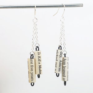 May include: Silver chain earrings with three book page charms. The charms are rolled up and have text from the book "To Kill a Mockingbird".