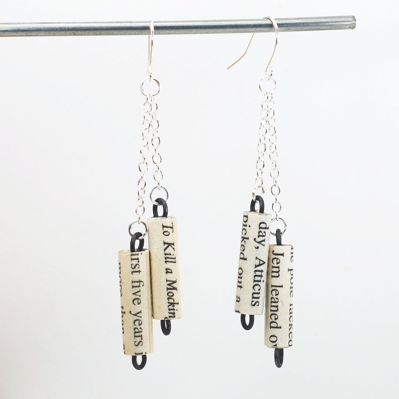 May include: Silver chain earrings with three book page charms. The charms are rolled up and have text from the book "To Kill a Mockingbird".