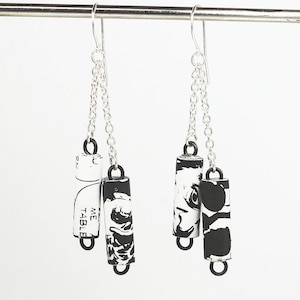 May include: Black and white patterned earrings with silver chains and black jump rings. The earrings are made from rolled up paper with the text "ME TABLED" visible.