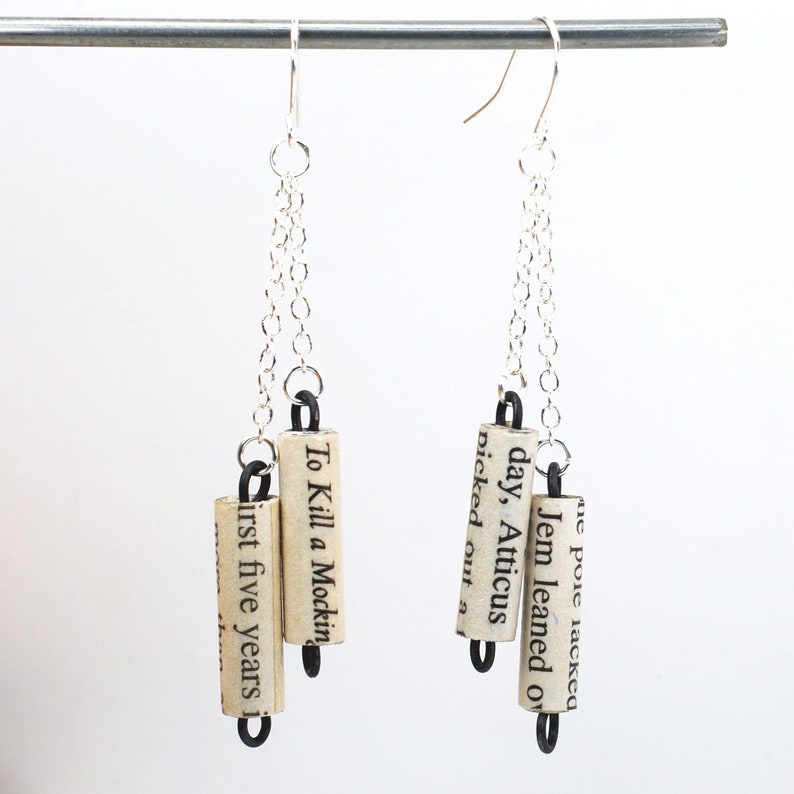 May include: Silver chain earrings with three dangling book page charms. The charms are made from rolled up pages of the book "To Kill a Mockingbird".
