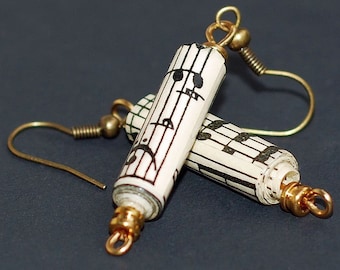 May include: A pair of gold tone earrings with a dangling cylinder charm made from rolled sheet music with black musical notes printed on it.