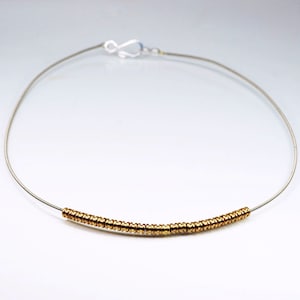Può includere: Una delicata collana d'oro con una semplice chiusura d'argento e una fila di piccole perle dorate.