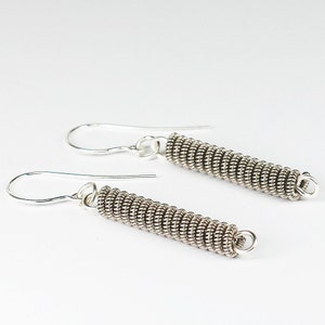 May include: A pair of silver earrings with a coiled wire design. The earrings are long and dangle from the earlobe.