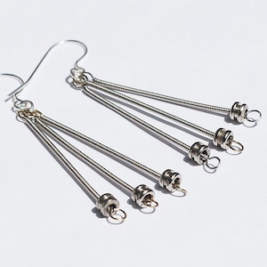 Puede incluir: Pendientes de aro de plata hechos con múltiples cuerdas de guitarra con pequeños anillos de plata en el extremo de cada cuerda.