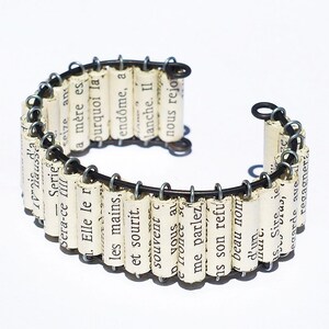 May include: A bracelet made of rolled up pages of a book, with the text visible, connected by wire. The bracelet is open and ready to be worn.