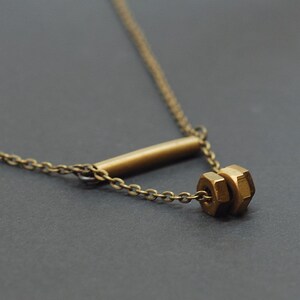 May include: A gold necklace with a bar and a cluster of nuts as the pendant.