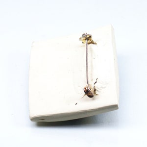 May include: White ceramic brooch with a pin on the back. The pin is made of metal and has a gold finish.