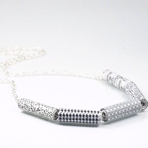 May include: A silver chain necklace with five black and white patterned cylinder beads. The beads have different geometric patterns.