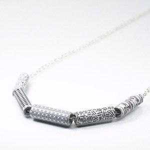 May include: A silver chain necklace with four black and white patterned cylinder beads. The beads have different geometric designs.