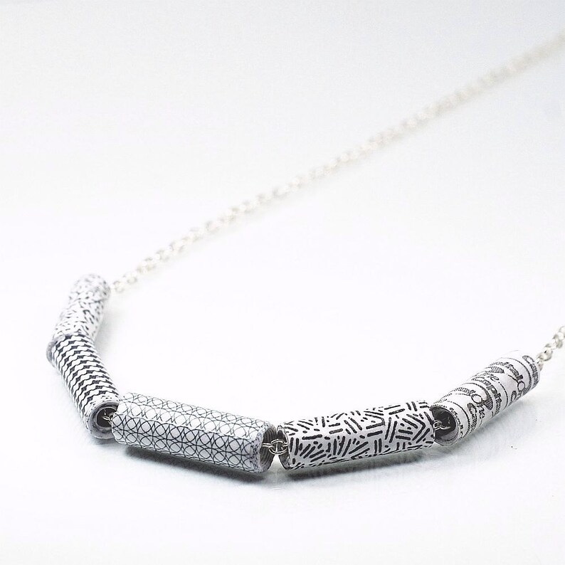 May include: A silver chain necklace with four black and white patterned cylinder beads. The beads have different geometric designs.
