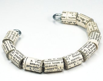 May include: A bracelet made of rolled-up pages from a book. The pages are connected with metal clasps. The bracelet is a light beige color.