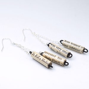 May include: Silver earrings with a chain and three small paper scroll charms. The charms are made from pages of the book "To Kill a Mockingbird" and feature text from the book.