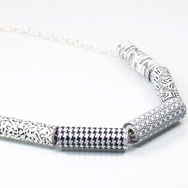 May include: A white necklace with a silver chain and five black and white patterned cylinder beads.