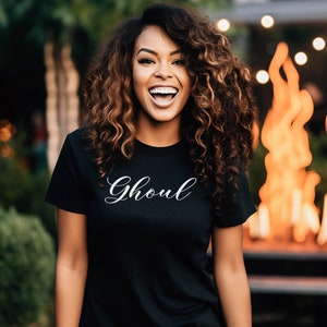 May include: A black t-shirt with the word "Ghoul" written in white cursive script.