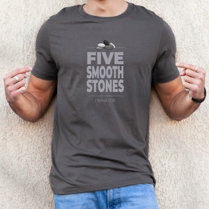 May include: A dark gray t-shirt with a graphic of five smooth stones and the text "FIVE SMOOTH STONES" and "1 Samuel 17:20".