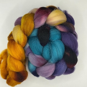 May include: A colorful braid of wool roving in shades of gold, teal, purple, and black. The fiber is tightly twisted, showcasing a gradient of colors. This craft supply is ideal for spinning, felting, or other fiber arts projects.