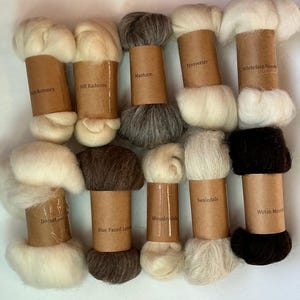May include: Ten bundles of raw wool fiber, each wrapped in a brown paper label with printed text identifying the breed. The collection includes various shades of white, cream, gray, brown, and black wool, arranged in two rows of five bundles.