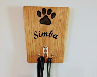 Puede incluir: Porta-correas de perro de madera con dos ganchos, un diseño de huella de pata y el nombre "Simba" grabado en él.