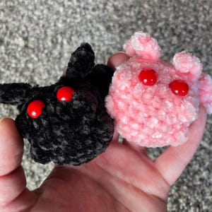 May include: Two crocheted plush toys with red button eyes. One is black and the other is pink.