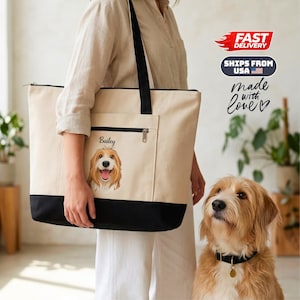 Op de afbeelding: Een beige canvas draagtas met een zwart bodempaneel en zwarte schouderbanden. De voorkant heeft een ritsvak met een gedrukte illustratie van een goudbruine hond en de naam Bailey in zwarte letters boven de hond.