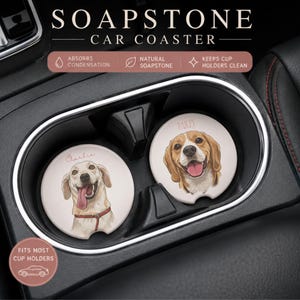 May include: Two round soapstone car coasters featuring illustrations of dogs. One coaster shows a light-colored dog with the name Charlie, and the other shows a beagle-type dog with the name Bailey. The text SOAPSTONE CAR COASTER is visible.