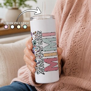 Könnte beinhalten: Ein weißer zylindrischer Becher mit einem Blumenmuster und dem vertikal angeordneten Text "blessed to be called MIMI". Der Becher enthält einen durchsichtigen Deckel und einen transparenten Strohhalm, mit dem Text "STRAW INCLUDED" darüber.