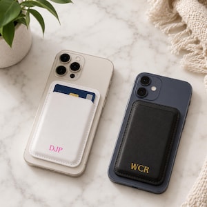 May include: A light-colored smartphone with a white magnetic card holder featuring the pink monogram DJP, and a dark blue smartphone with a black magnetic card holder featuring the gold monogram WCR, both attached to the back of the devices.
