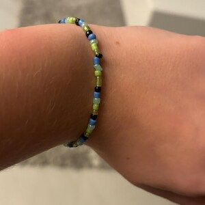 K&ouml;nnte beinhalten: Ein Armband mit schwarzen, blauen, gr&uuml;nen und hellgr&uuml;nen Perlen.