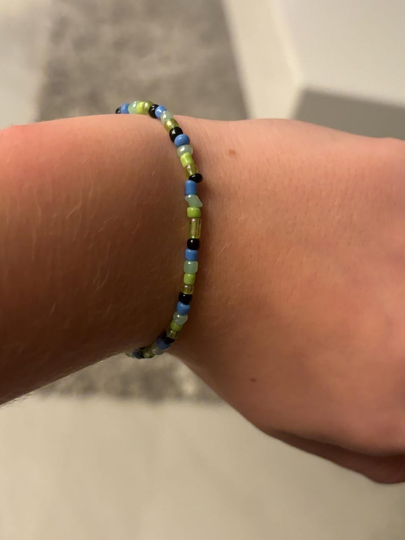 K&ouml;nnte beinhalten: Ein Armband mit schwarzen, blauen, gr&uuml;nen und hellgr&uuml;nen Perlen.