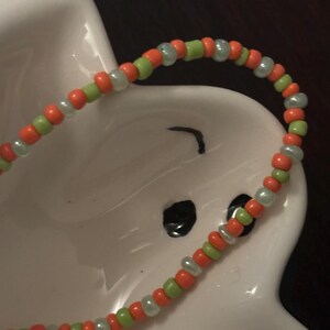 Könnte beinhalten: Nahaufnahme eines Armbands mit abwechselnd orangefarbenen, grünen und weißen Perlen.