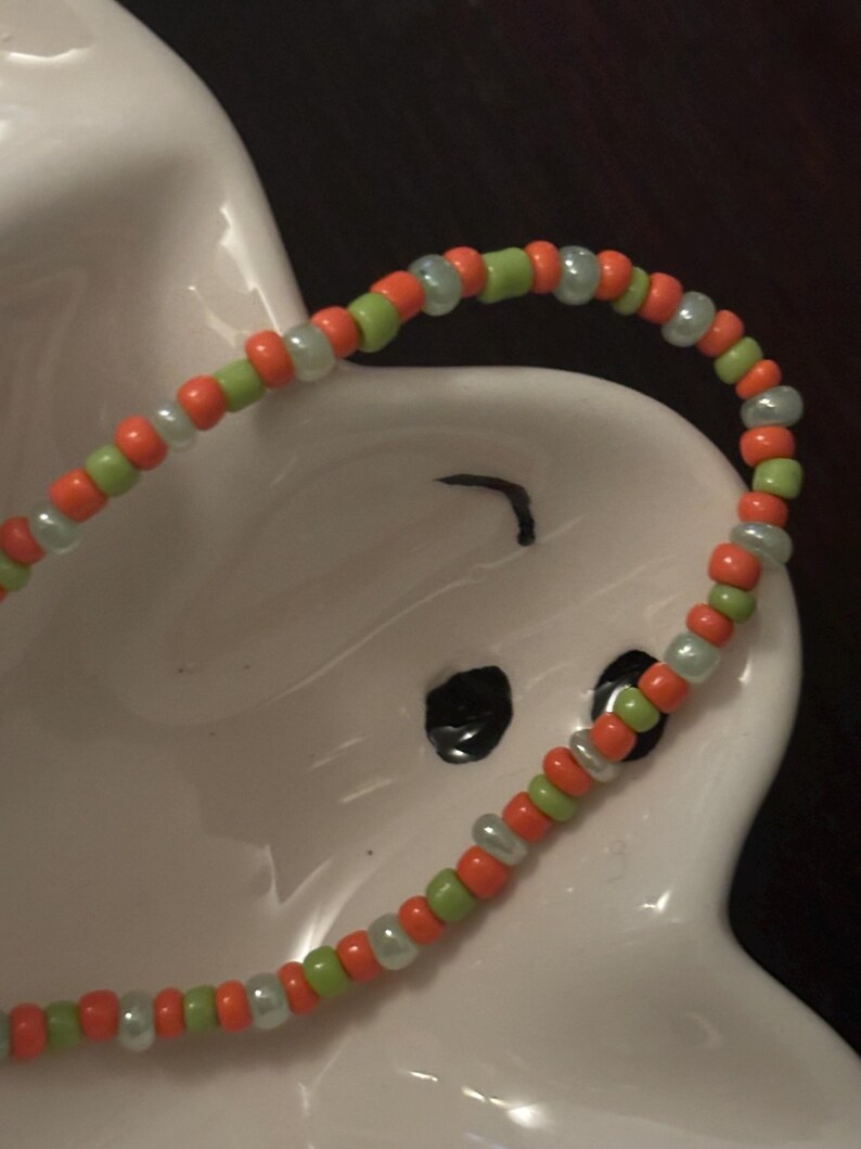 K&ouml;nnte beinhalten: Nahaufnahme eines Armbands mit abwechselnd orangefarbenen, gr&uuml;nen und wei&szlig;en Perlen.