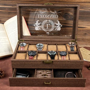 Puede incluir: Una caja de madera para relojes con tapa de cristal y un cajón. La caja tiene una inscripción personalizada que dice "GEOLIVKD G". La caja tiene 12 ranuras para relojes y un cajón para guardar joyas.