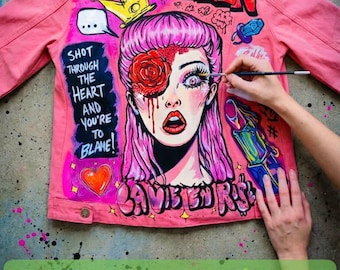 May include: A pink denim jacket featuring a hand-painted graphic of a person with pink hair, a red rose over one eye, and the text "THE QUEEN," "SHOT THROUGH THE HEART AND YOU'RE TO BLAME!," and "LA VIE EN ROSE" in bold, colorful lettering.