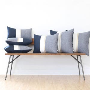 Op de afbeelding: Een houten bank met vijf decoratieve kussens. De kussens zijn gestreept met donkerblauwe, witte en beige stof.