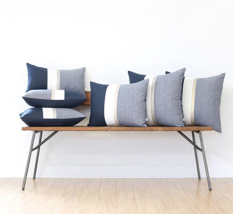 Op de afbeelding: Een houten bank met vijf decoratieve kussens. De kussens zijn gestreept met donkerblauwe, witte en beige stof.