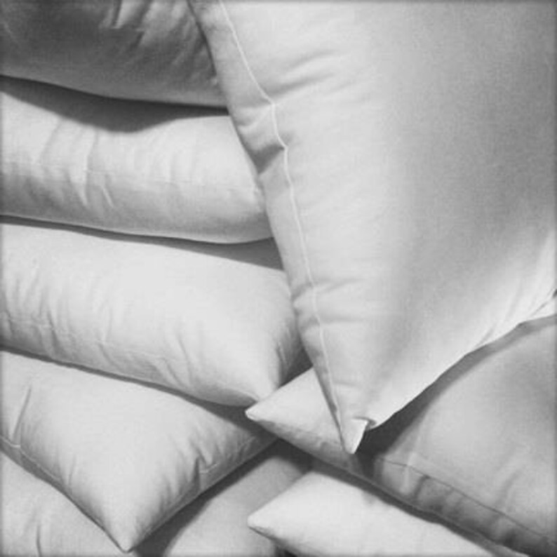 May include: A stack of white pillows, arranged in a pyramid shape. The pillows are made of a soft, fluffy material and have a smooth, white fabric cover.
