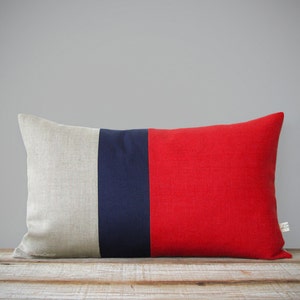 May include: A rectangular pillow with a linen fabric cover. The pillow is divided into three vertical stripes: beige, navy blue, and red.