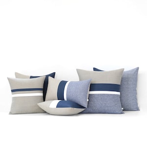 May include: Five decorative throw pillows with a striped pattern in shades of beige, white, and blue. The pillows are arranged in a row on a white surface.