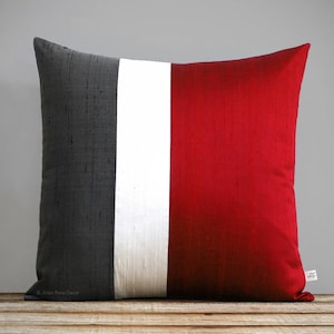 May include: A decorative pillow with a gray, white, and red striped design. The pillow is made of a soft, textured fabric.