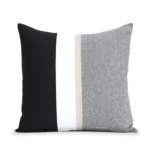 Puede incluir: Una almohada decorativa con un dise&ntilde;o de rayas negras, blancas y grises. La almohada est&aacute; hecha de una tela suave y texturizada.