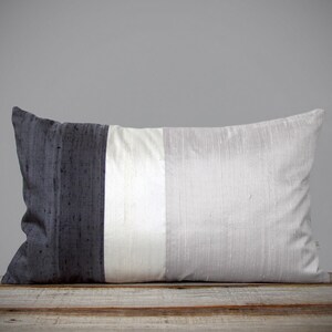 May include: A long rectangular pillow with a black, white, and gray striped design. The pillow is made of a soft, silky fabric.