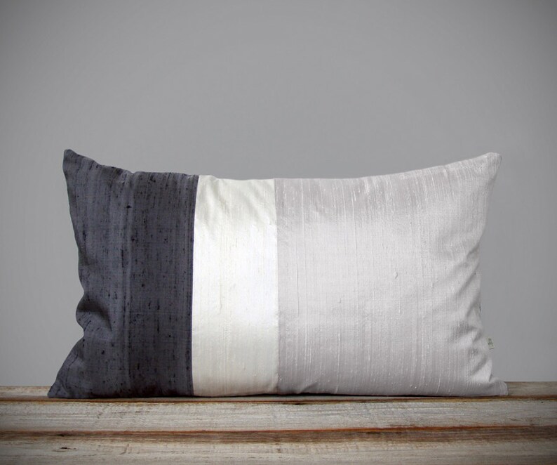 May include: A long rectangular pillow with a black, white, and gray striped design. The pillow is made of a soft, silky fabric.
