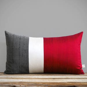 May include: A long rectangular pillow with a gray, white, and red striped design. The pillow is made of a textured fabric.