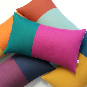 May include: Five colorful throw pillows with different color combinations. The pillows are made of a soft, textured fabric. The colors are orange, teal, pink, navy blue, and mustard yellow.