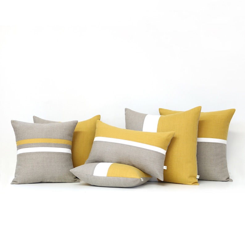 May include: A set of five decorative throw pillows with a modern geometric design. The pillows are made of a soft, textured fabric and feature a combination of gray and yellow colors with white stripes.