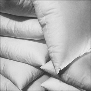 May include: A stack of white pillows, arranged in a pyramid shape. The pillows are made of a soft, fluffy material and have a smooth, white fabric cover.