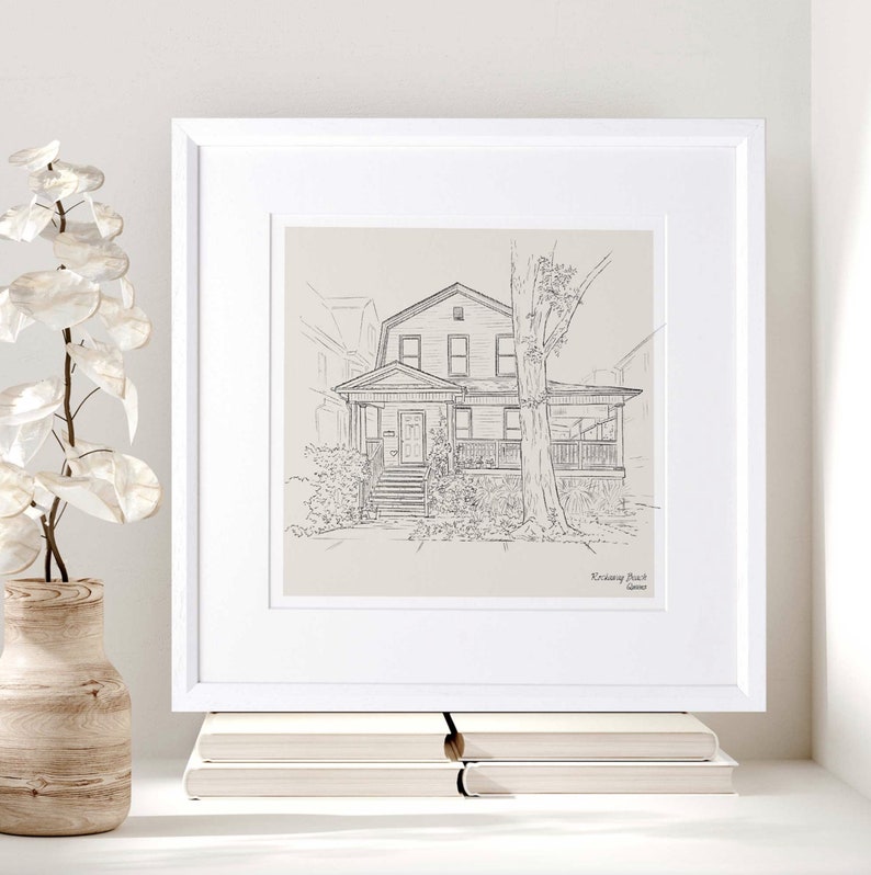 K&ouml;nnte beinhalten: Eine gerahmte Schwarz-Wei&szlig;-Skizze eines Hauses mit Veranda und Baum. Das Kunstwerk befindet sich in einem wei&szlig;en Rahmen und wird auf einer wei&szlig;en Oberfl&auml;che mit einer Vase und B&uuml;chern ausgestellt.