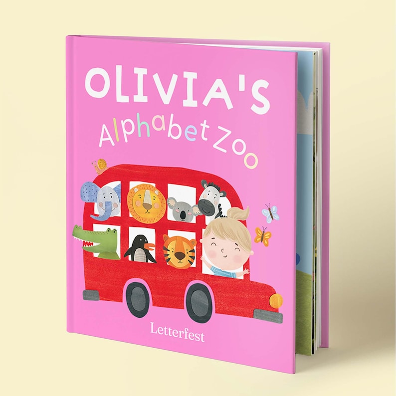 May include: A pink hardcover children's book titled OLIVIA'S ALPHABET ZOO. The cover features a red bus filled with illustrated animals including an elephant, lion, koala, zebra, crocodile, penguin, and tiger, alongside a child and butterflies.