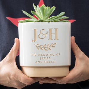 May include: White ceramic planter with a succulent plant. The planter is engraved with the initials "J&H" and the text "The Wedding of James and Helen".